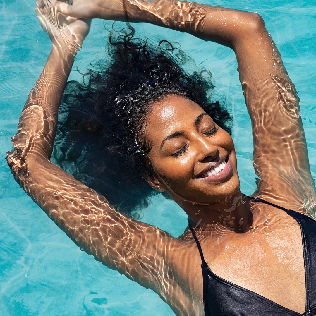 High angle view of black woman relaxing in the water with closed eyes. Portrait of happy woman in bikini floating in a water. Top view of relaxed african girl in swimming pool with copy space.